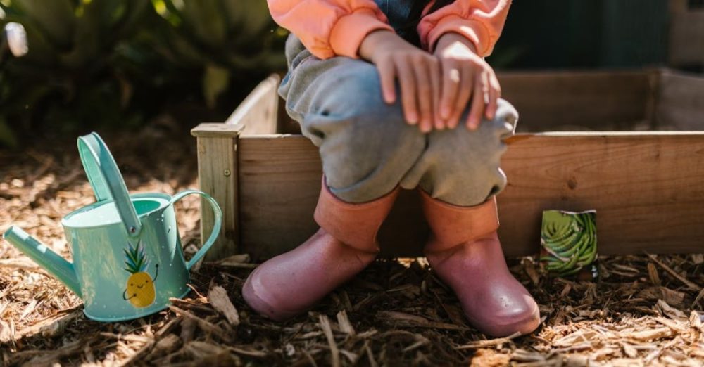 Mulching - A Child Sitting in Rubber Boots Sitting on a Wooden Plant Box