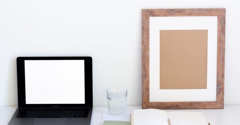 Watering Schedule - Laptop with blank screen and glass of water placed on white desk near empty frame and blank notepad against white wall