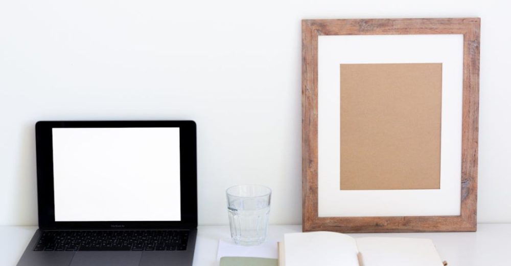 Watering Schedule - Laptop with blank screen and glass of water placed on white desk near empty frame and blank notepad against white wall