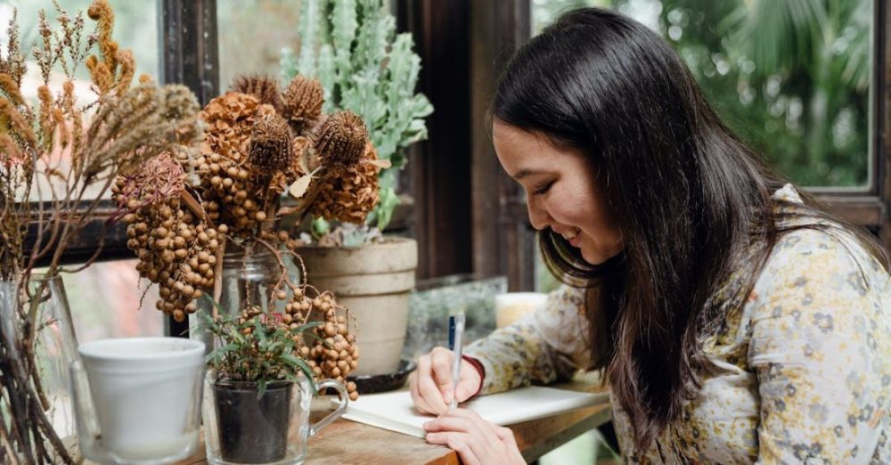 Garden Plan - Happy young ethnic woman writing article in cozy workplace