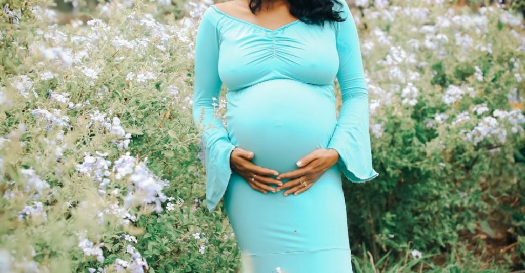 Flowering Shrubs - Pregnant Woman Standing by Flowering Shrubs Holding Her Belly